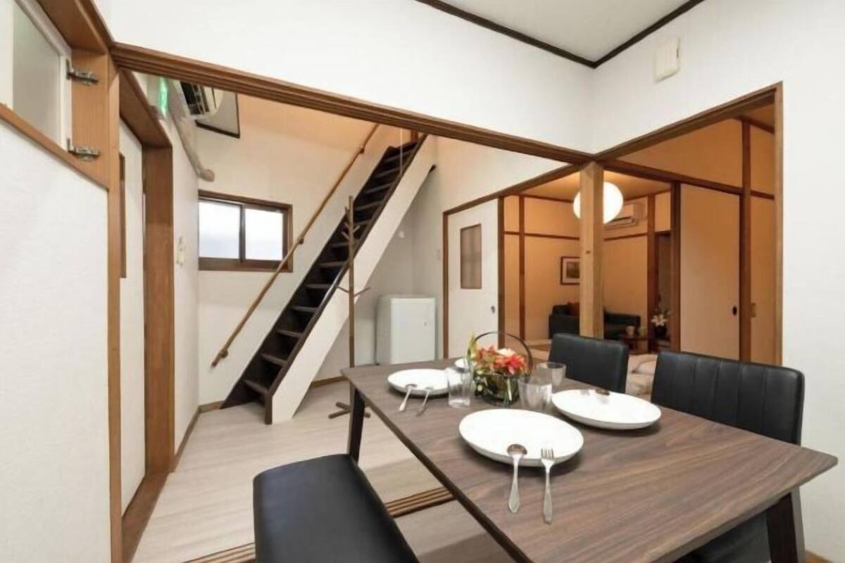 A dining area with a table set for four, a staircase, and a view into another room.