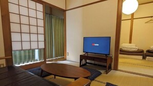 Une pièce de style japonais traditionnel, avec un sol recouvert de tatamis, une table basse, un téléviseur et une porte coulissante.