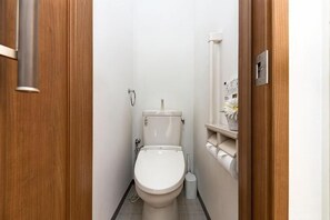 A narrow bathroom with a toilet, a wooden door, and a wall-mounted light fixture. - Kiyomizu Dongurian (Kyoto)
