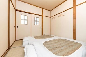 A traditional Japanese-style room with tatami flooring, a futon bed, sliding doors, and a hanging clothes rack. - Kiyomizu Dongurian (Kyoto)