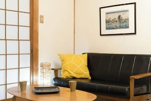 A room with a black leather sofa, a wooden table, a yellow pillow, and a framed picture on the wall.