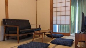 Une pièce de style japonais traditionnel, avec un sol recouvert de tatamis, un canapé en cuir noir, une petite table en bois et une porte coulissante de type shoji.