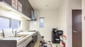 A narrow kitchen with a window, a sink, cabinets, and a fire extinguisher. - CROWN Umibe (Tokyo)