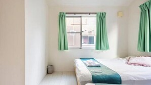 A room with two beds, a window with green curtains, and a visible trash bin. - CROWN Umibe (Tokyo)