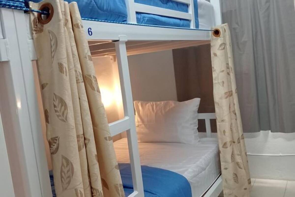 A bunk bed with a number '6' on the side, a blue mattress, and beige curtains with leaf patterns.