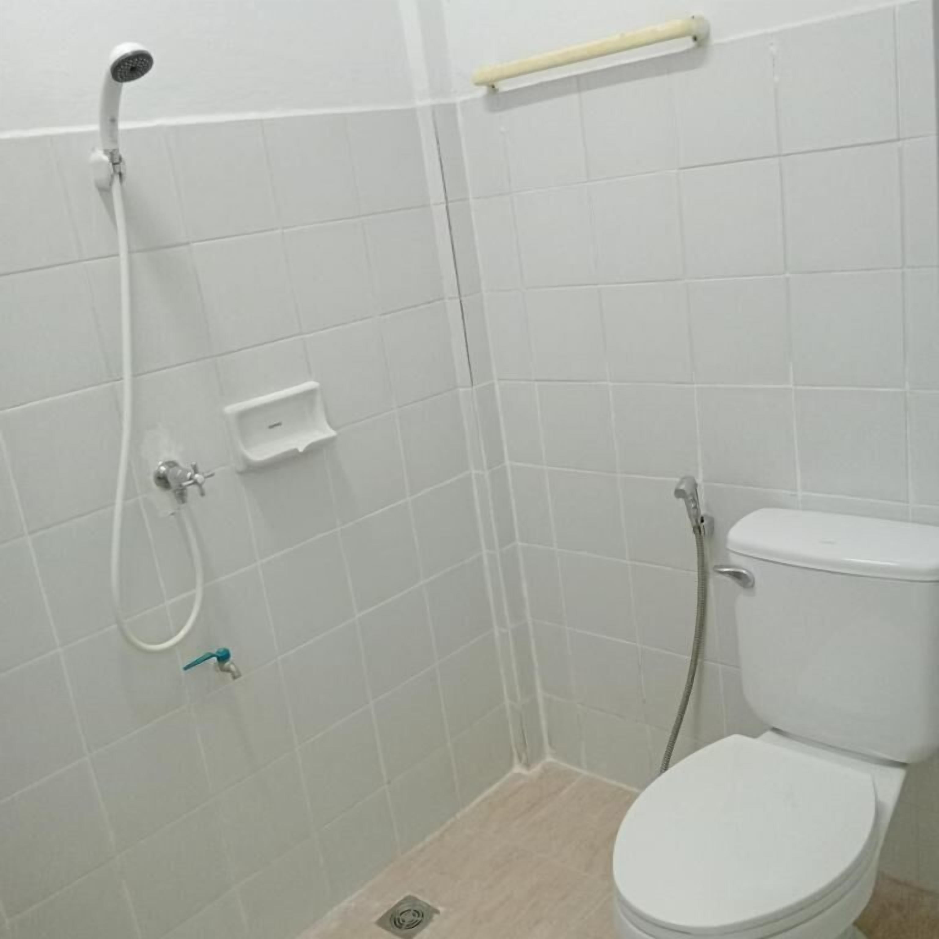 A small, white-tiled bathroom with a toilet, a shower, and a soap dish.