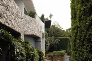 A modern building with a stone facade, a green hedge, and a well-maintained garden. - KW VILLA (Koh Samui)