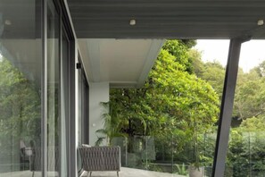 A modern outdoor seating area with a glass enclosure, a potted plant, and a view of lush greenery. - KW VILLA (Koh Samui)