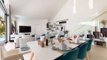 Een moderne woonkamer met een eethoek, een televisie en een keuken op de achtergrond.