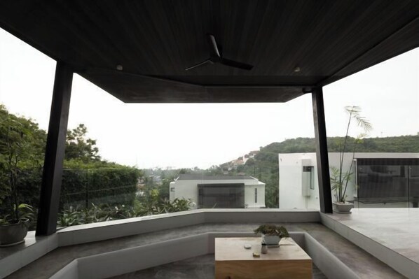 A modern outdoor space with a wooden table, potted plants, and a view of surrounding buildings. - KW VILLA (Koh Samui)