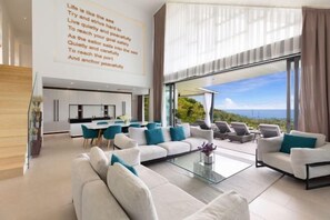 A modern living room with a large glass wall, a sofa set, and a dining area. - KW VILLA (Koh Samui)