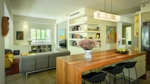 A modern kitchen with a wooden island, black bar stools, and a vase of flowers. - Spacious & Green 3BR Apt w Balcony in City Center (Tel Aviv)