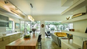 A modern kitchen with a wooden island, bar stools, and a yellow sofa. - Spacious & Green 3BR Apt w Balcony in City Center (Tel Aviv)