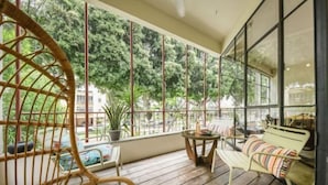 A wooden deck with a wicker chair, a bench with a striped cushion, and a table with a vase. - Spacious & Green 3BR Apt w Balcony in City Center (Tel Aviv)