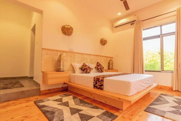 Ein Schlafzimmer mit Bett, Nachttischen, einem Fenster und Blick auf Grün.