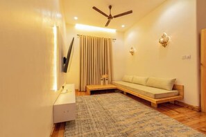 Ein Zimmer mit Deckenventilator, einer Couch, einem an der Wand befestigten Fernseher und einem gemusterten Teppich.