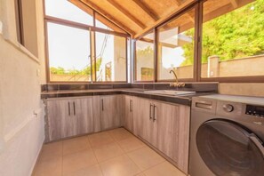 A compact kitchen with a built-in washing machine, large windows, and a tiled floor. - Jandi Diani (Diani Beach)