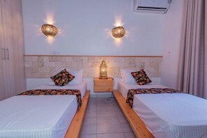 Ein Hotelzimmer mit zwei Betten, einem an der Wand befestigten Kopfteil mit Steinmuster und zwei Wandleuchten.