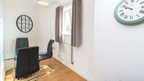 Ett modernt matområde med ett glasbord, svarta stolar, en rund väggklocka och ett fönster med gardiner.