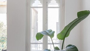 A room with a large window, a potted plant, and a view of a building outside. - The Gem of Neve Tzedek Stylish Home (Tel Aviv)