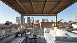A rooftop terrace with a wooden pergola, a white sofa, a round table, and potted plants. - The Gem of Neve Tzedek Stylish Home (Tel Aviv)