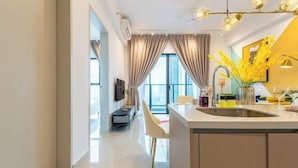 A modern kitchen with a central island, a dining area with a chair, and a large window with curtains. - Trion@KL by YourSuperhost (Kuala Lumpur)