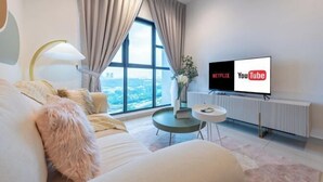 A modern living room with a large window, a sofa, a coffee table, and a TV displaying Netflix and YouTube logos. - Trion@KL by YourSuperhost (Kuala Lumpur)