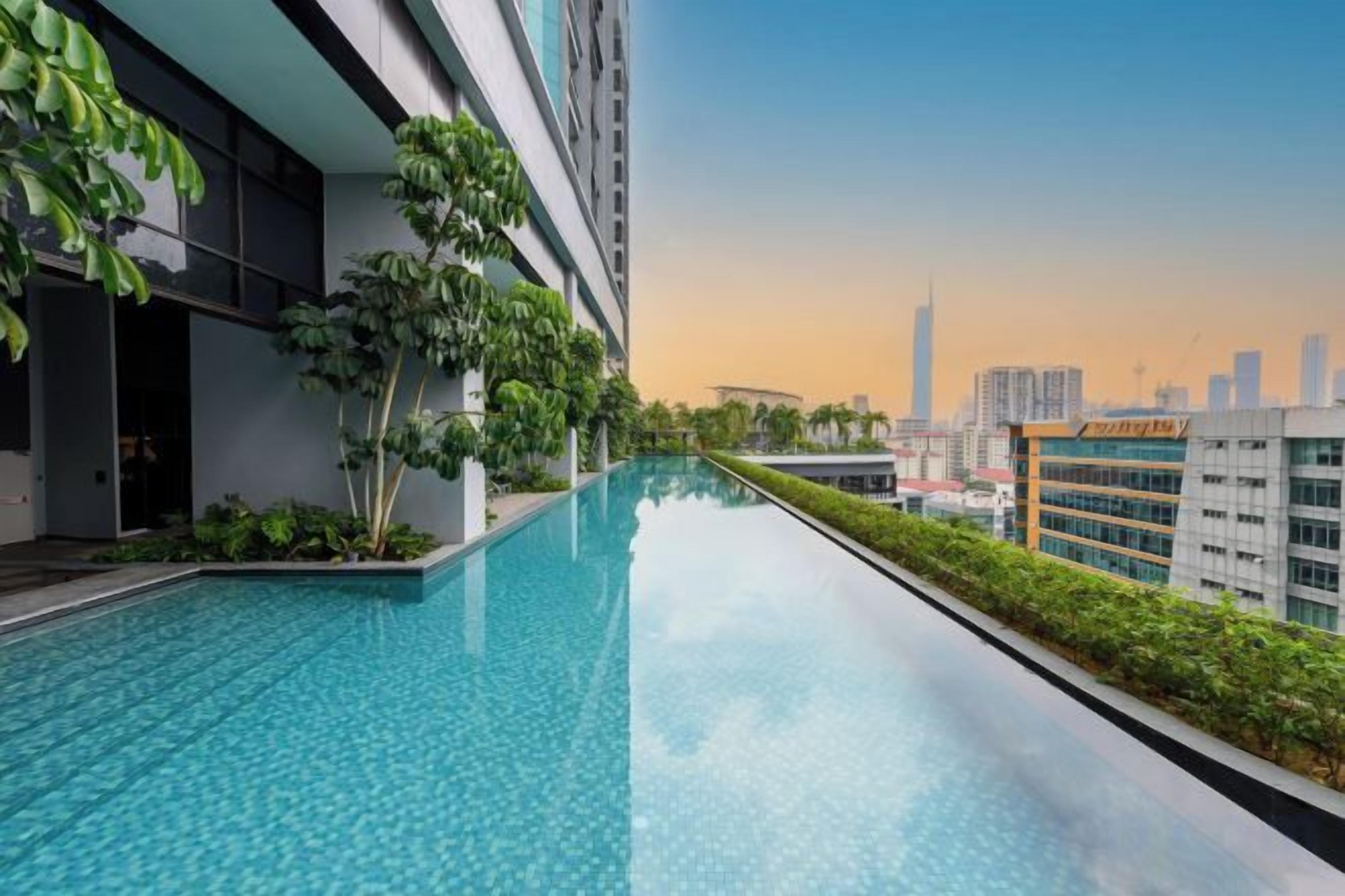 A rooftop infinity pool with a city skyline view, surrounded by greenery and modern buildings.