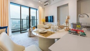A modern hotel room with a dining area, a large window with a city view, a flat-screen TV, and a minibar. - Trion@KL by YourSuperhost (Kuala Lumpur)