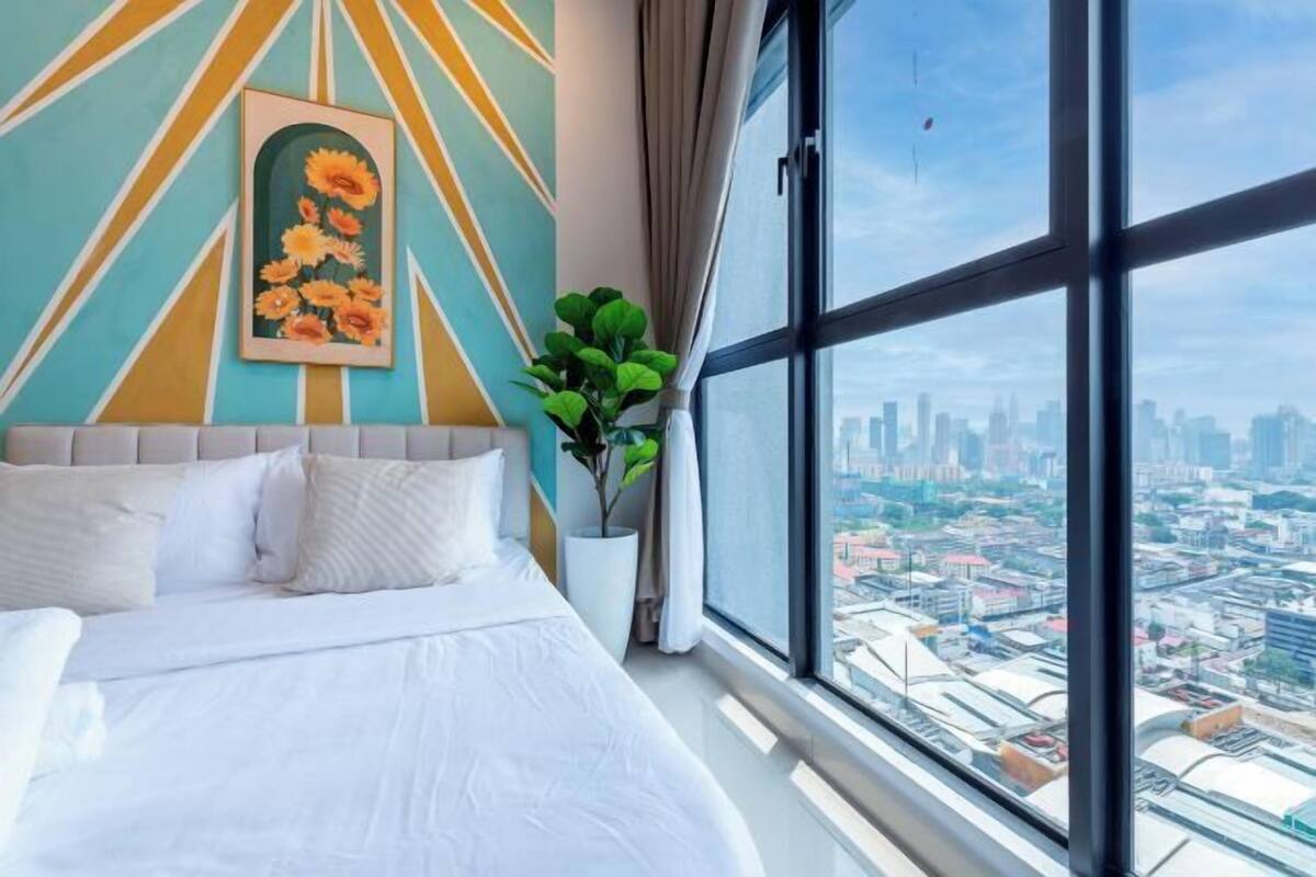 Una habitación de hotel moderna con una cama grande, vistas a la ciudad, un diseño geométrico en la pared y una planta en maceta.
