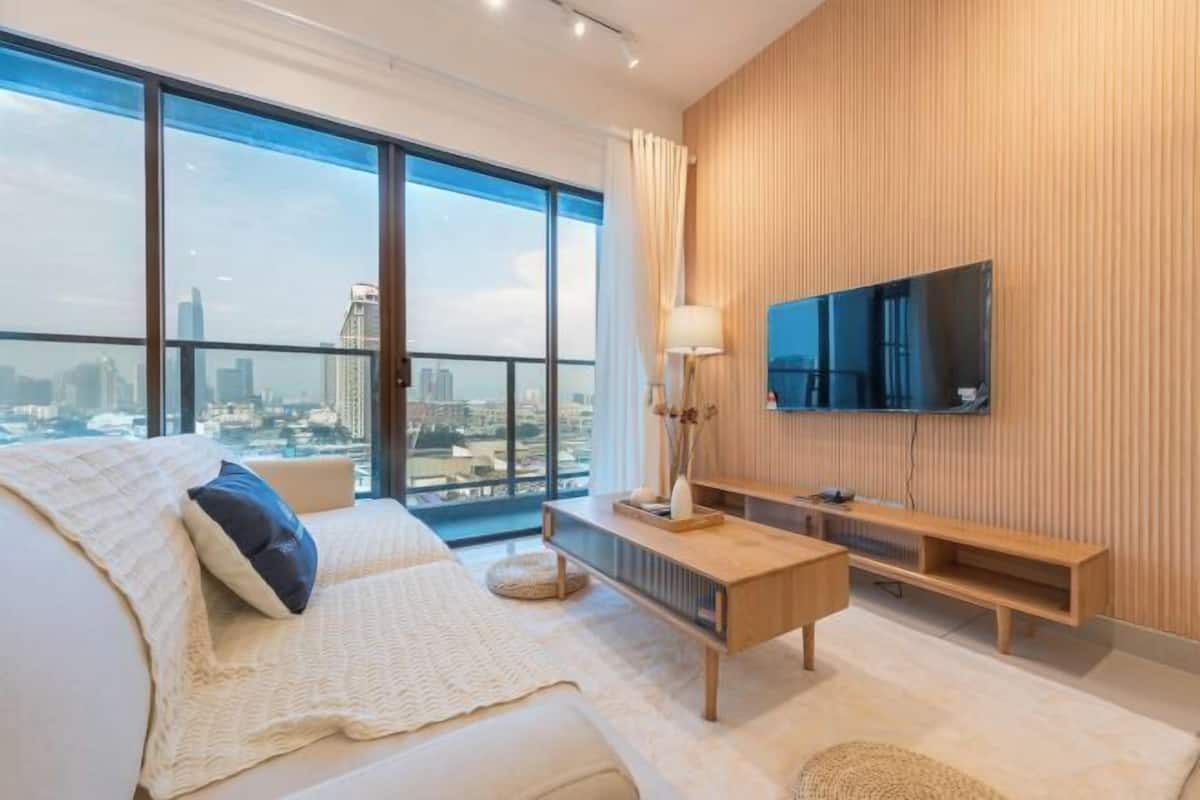 Una sala de estar moderna con un ventanal grande, un televisor de pantalla plana, una mesa consola de madera y un sofá.