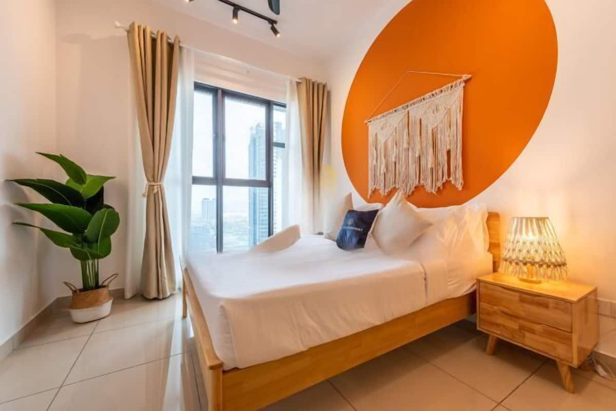 Un dormitorio moderno con una cama grande, una lámpara de noche, una planta en maceta y vistas de la ciudad.