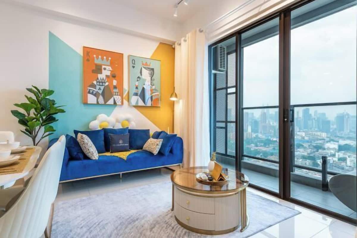 Un salon moderne avec un canapé bleu, une table basse ronde et une vue sur la ville grâce à de grandes fenêtres.