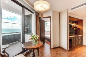 Une chambre d’hôtel moderne avec balcon, une table ronde en bois agrémentée d’un vase de fleurs et un coin cuisine intégré.