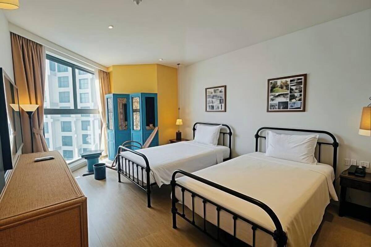A hotel room with two beds, a desk, a wardrobe, and a window with curtains.