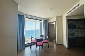 Une pièce comprenant une table et des chaises, un coin cuisine, et une porte donnant sur une autre pièce. La pièce offre également une vue sur la mer.