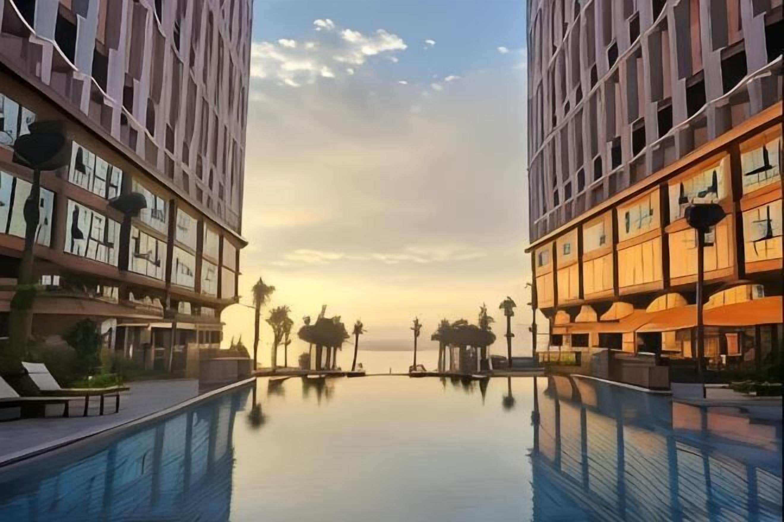 Un hotel moderno con piscina, palmeras y vistas al atardecer.
