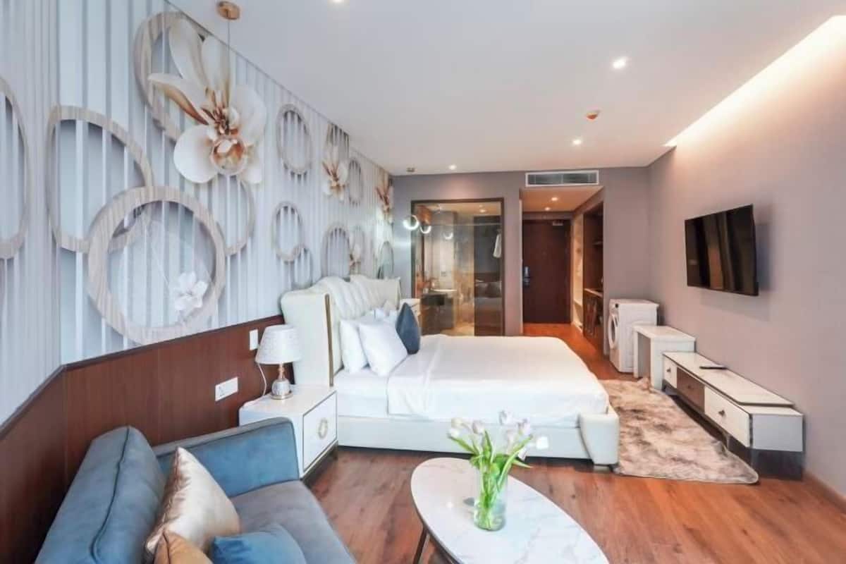 A modern hotel room with a large bed, a sofa, a small table, and a TV.