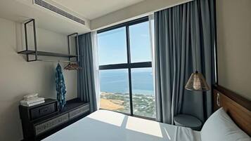 Habitación de hotel con un ventanal grande, una cama, una mesita de noche con lámpara y un espejo en la pared.