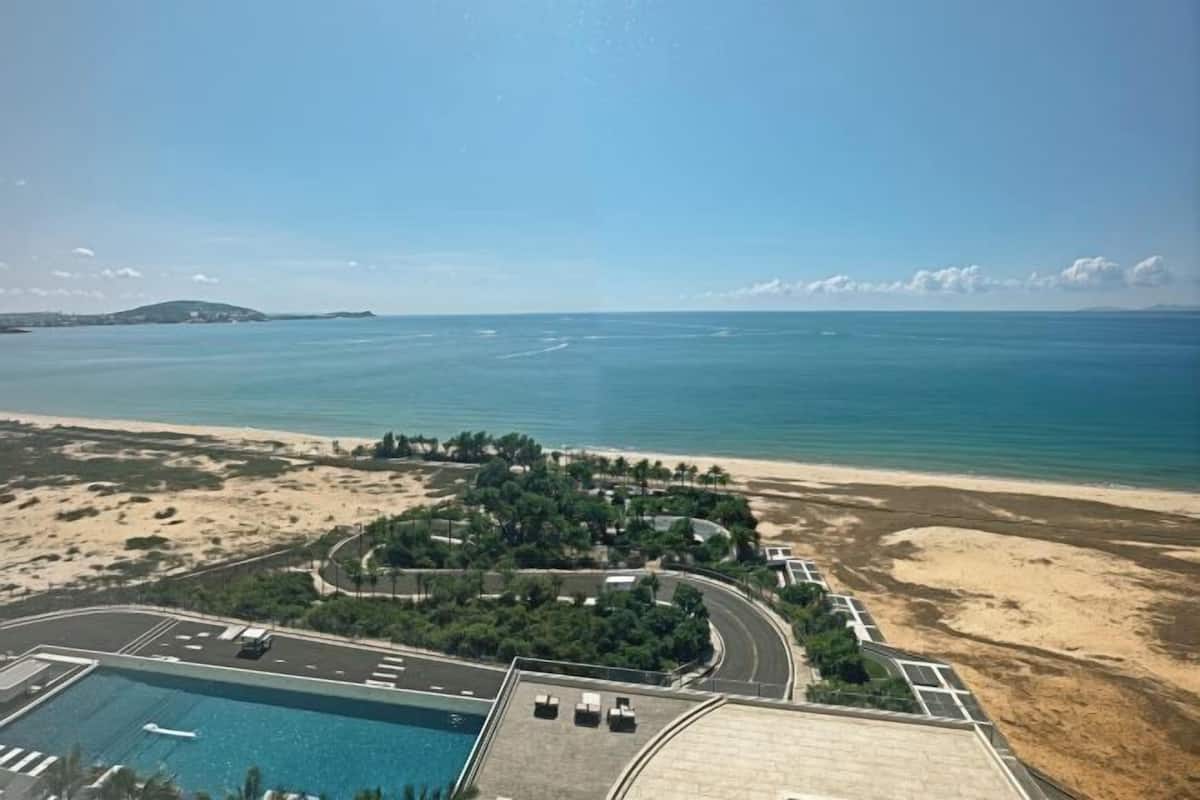 An aerial view of a coastal area with a beach, a parking lot, and a swimming pool.