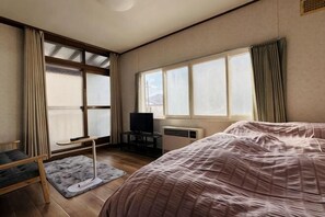A bedroom with a bed, a desk, a chair, a TV, and large windows. - SecondHouse Green (Otaru)