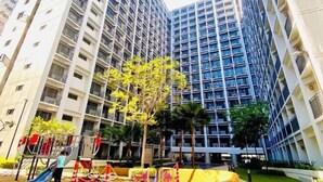 A high-rise residential building with multiple balconies, a playground with slides, and palm trees in the courtyard. - Ai-Stay 78 at Shore 2 T1 (Pasay)