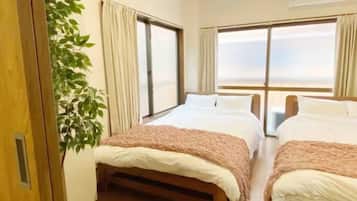 A hotel room with two beds, a large window, and a potted plant.