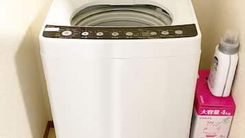A front-loading washing machine with a control panel and a detergent bottle beside it.