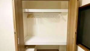 A walk-in closet with a wooden door, a white shelf, and a hanging rod. - SunStay Tachiaikawa II (Tokyo)