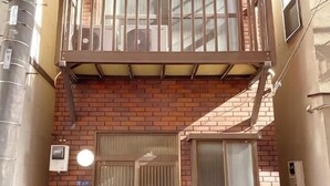 A brick building with a metal balcony, a door, and a window. - SunStay Tachiaikawa II (Tokyo)