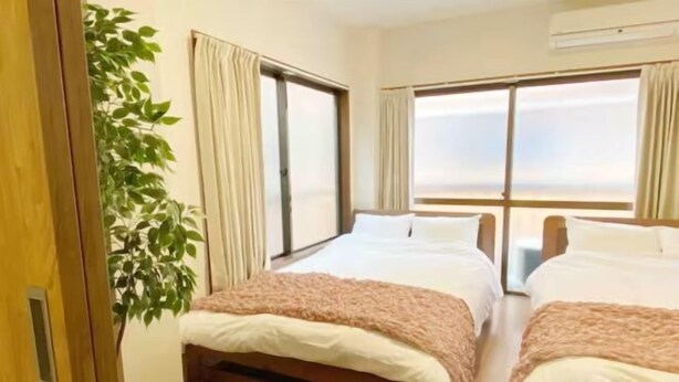 A room with two beds, a large window, and a potted plant. - SunStay Tachiaikawa II (Tokyo)