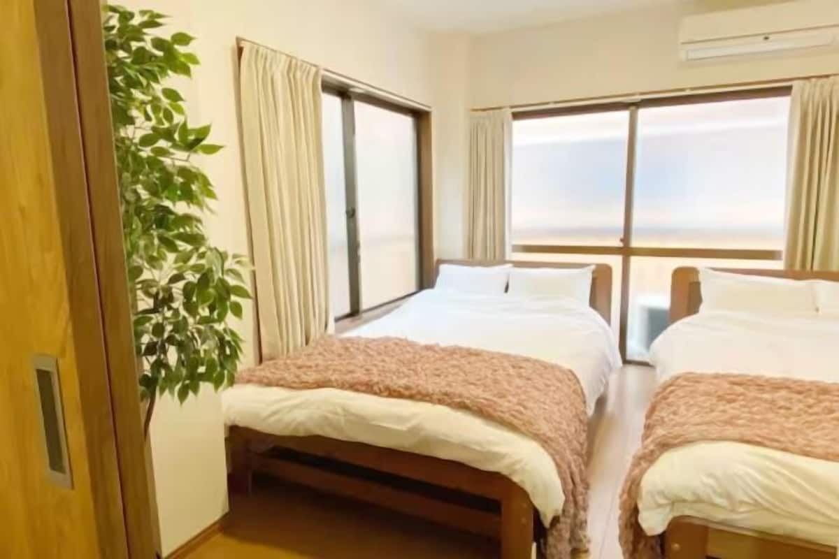 A room with two beds, a large window, and a potted plant.
