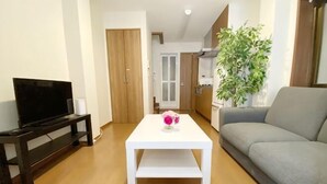A living room with a sofa, a TV on a stand, a white table, and a plant. - SunStay Tachiaikawa II (Tokyo)