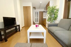 A living room with a sofa, a TV on a stand, a white table, and a plant. - SunStay Tachiaikawa II (Tokyo)